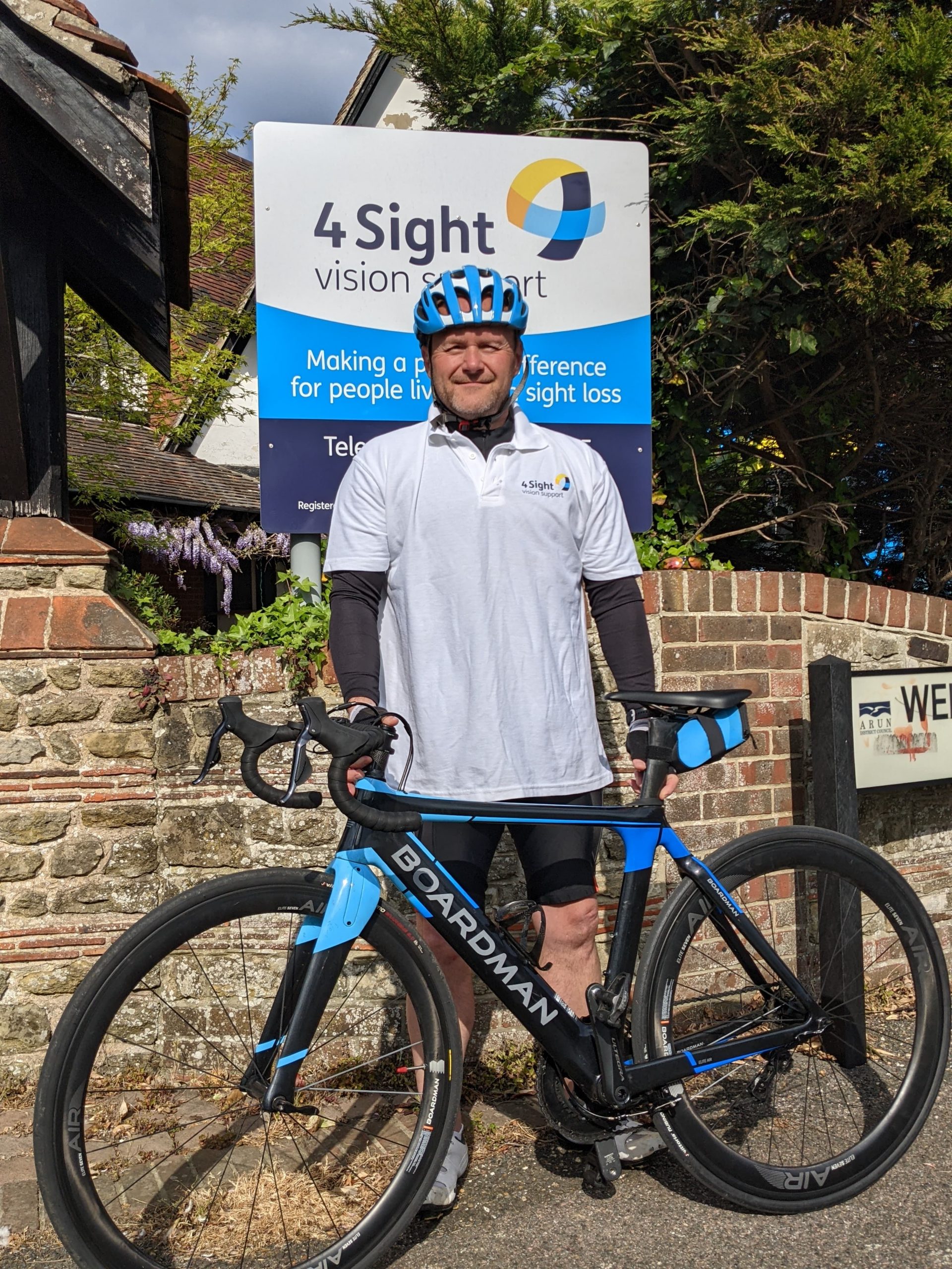 Image of Rob wearing his cycling gear complete with a blue helmet holding his blue bike as he stands in front of the 4Sight offices in Bognor Regis.