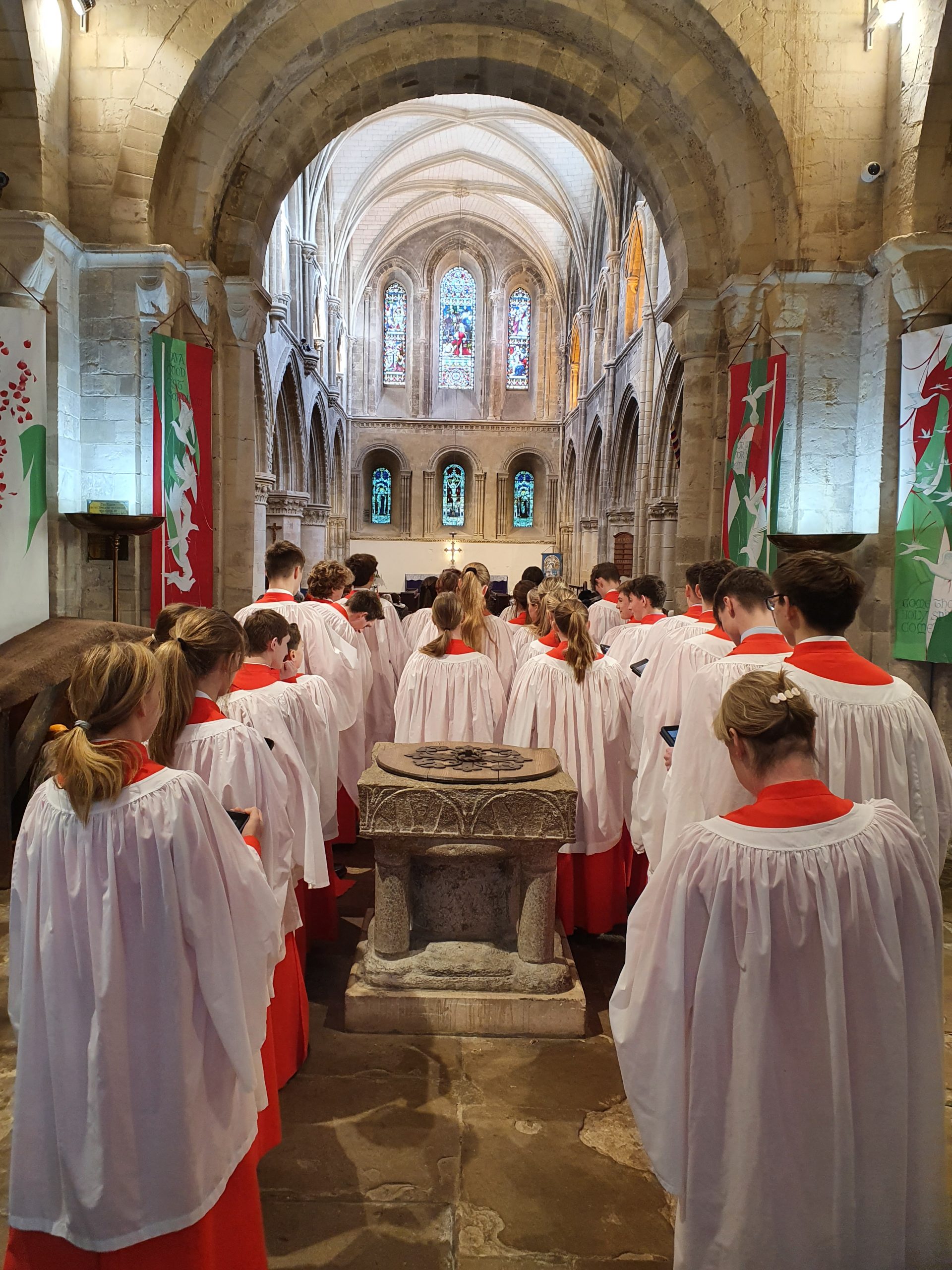 Seaford Chapel choir in their white and red robes singing in a traditional looking stone church building as the walk down the central isle towards the front..
